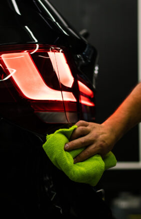 A selective focus shot of a man cleaning car's back headlight with a microfiber cloth